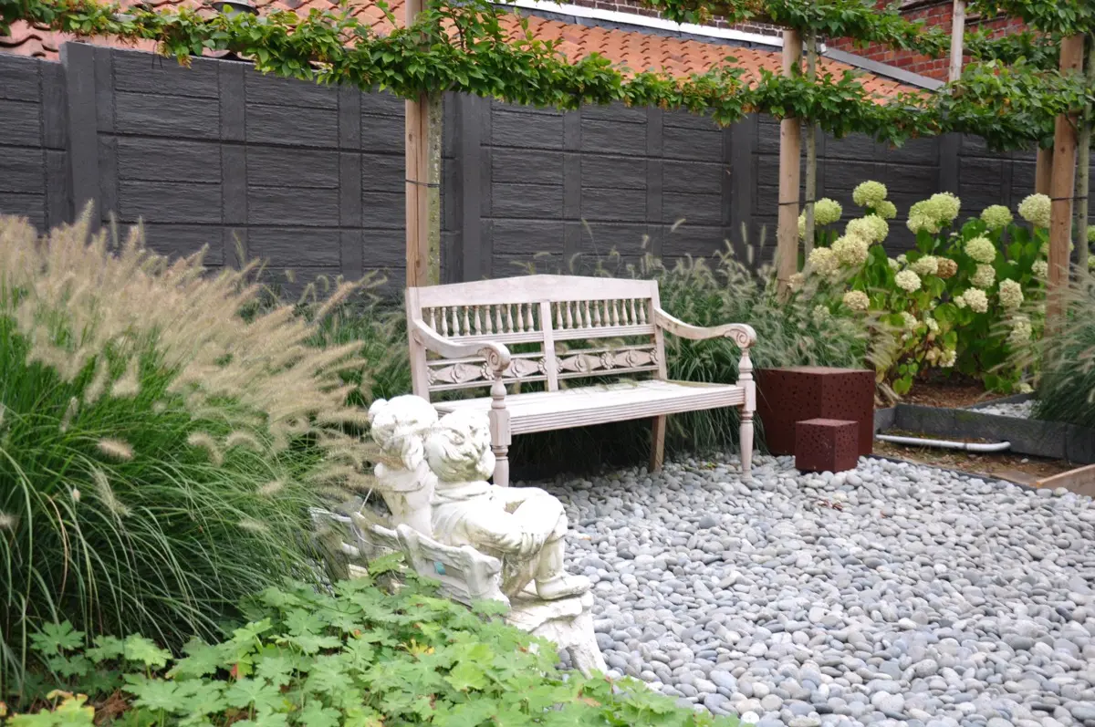 Anthrazitfarbener Betonzaun Motiv Nordic hinter einer Gartenbank mit Kiesbeet